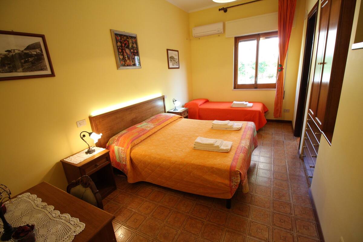 A hotel room with two beds, a desk with a lamp, a chair, and a window with curtains.