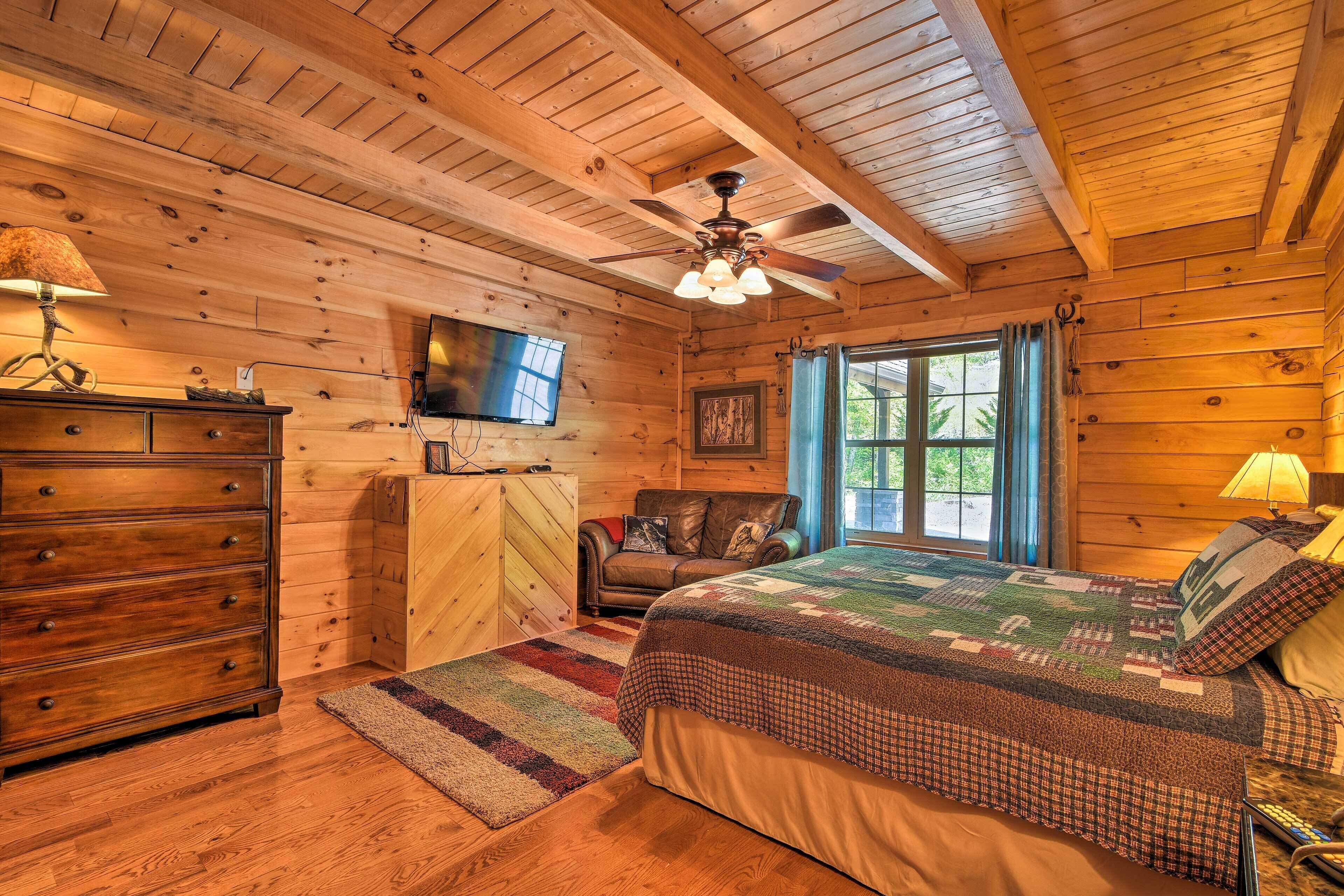 Une chambre dans une cabane en bois, avec un lit, une commode, une télévision et un ventilateur de plafond.
