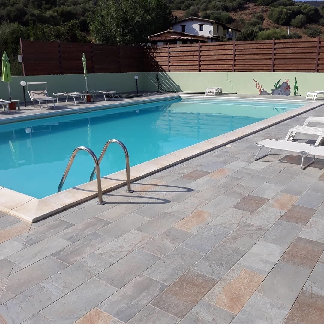 A swimming pool with a tiled deck, lounge chairs, and a wooden fence in the background.