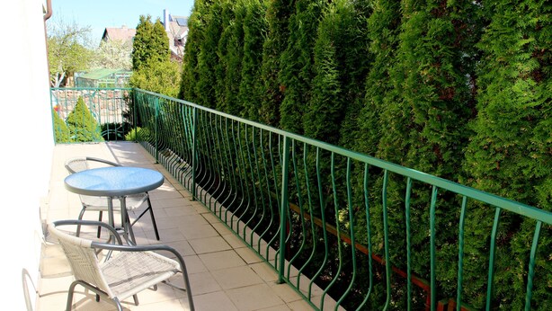A balcony with a green metal railing, two round tables, and two wicker chairs. - Klaipeda-Apartments (Klaipeda)