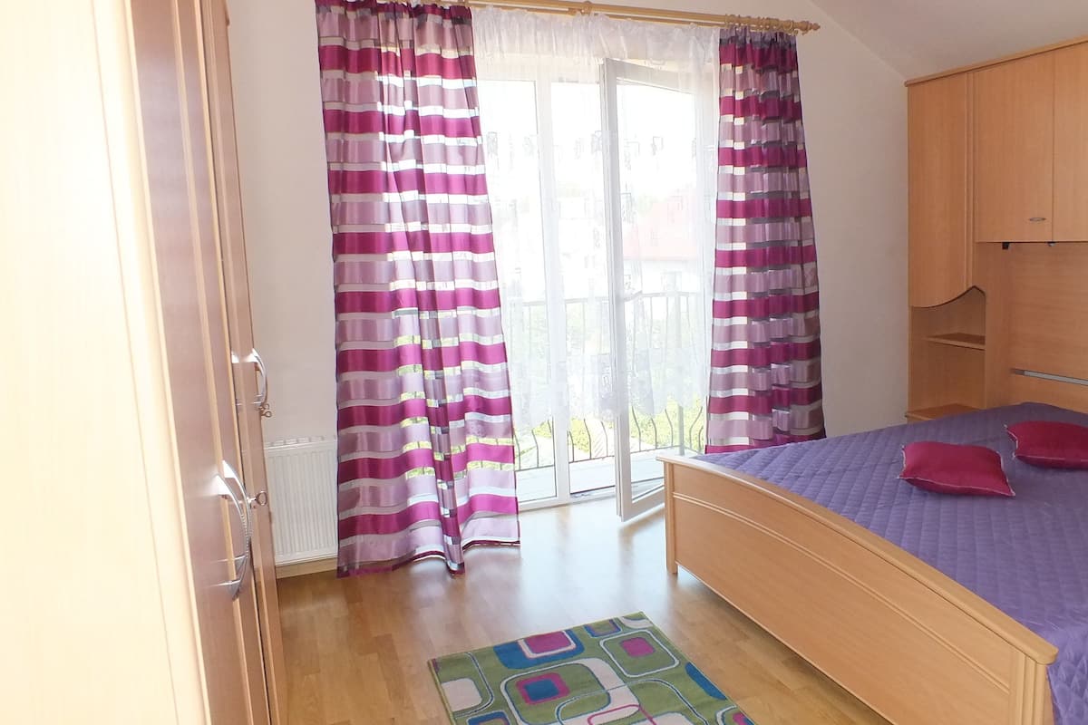 A bedroom with a bed, wooden wardrobe, and a window with curtains.