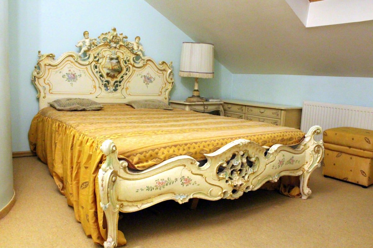 A bedroom with a classic bed, a nightstand, a lamp, and a chest of drawers.