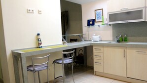 A compact kitchen with a small dining area, including a counter, two chairs, and basic amenities like a microwave and a sink. - Klaipeda-Apartments (Klaipeda)