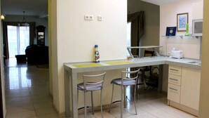 A kitchen with a bar counter, two bar stools, a microwave, and a window with curtains. - Klaipeda-Apartments (Klaipeda)