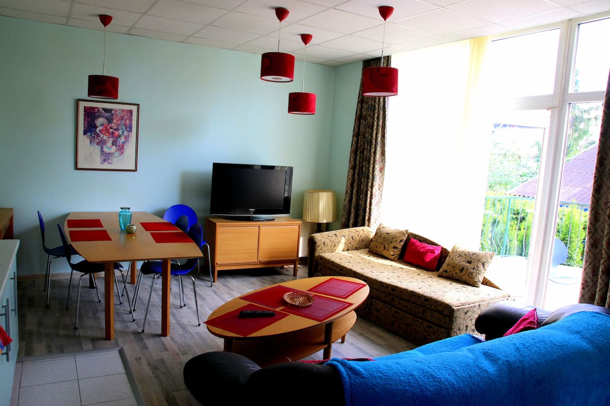 A living room with a TV, sofa, dining table, chairs, and a window with curtains.