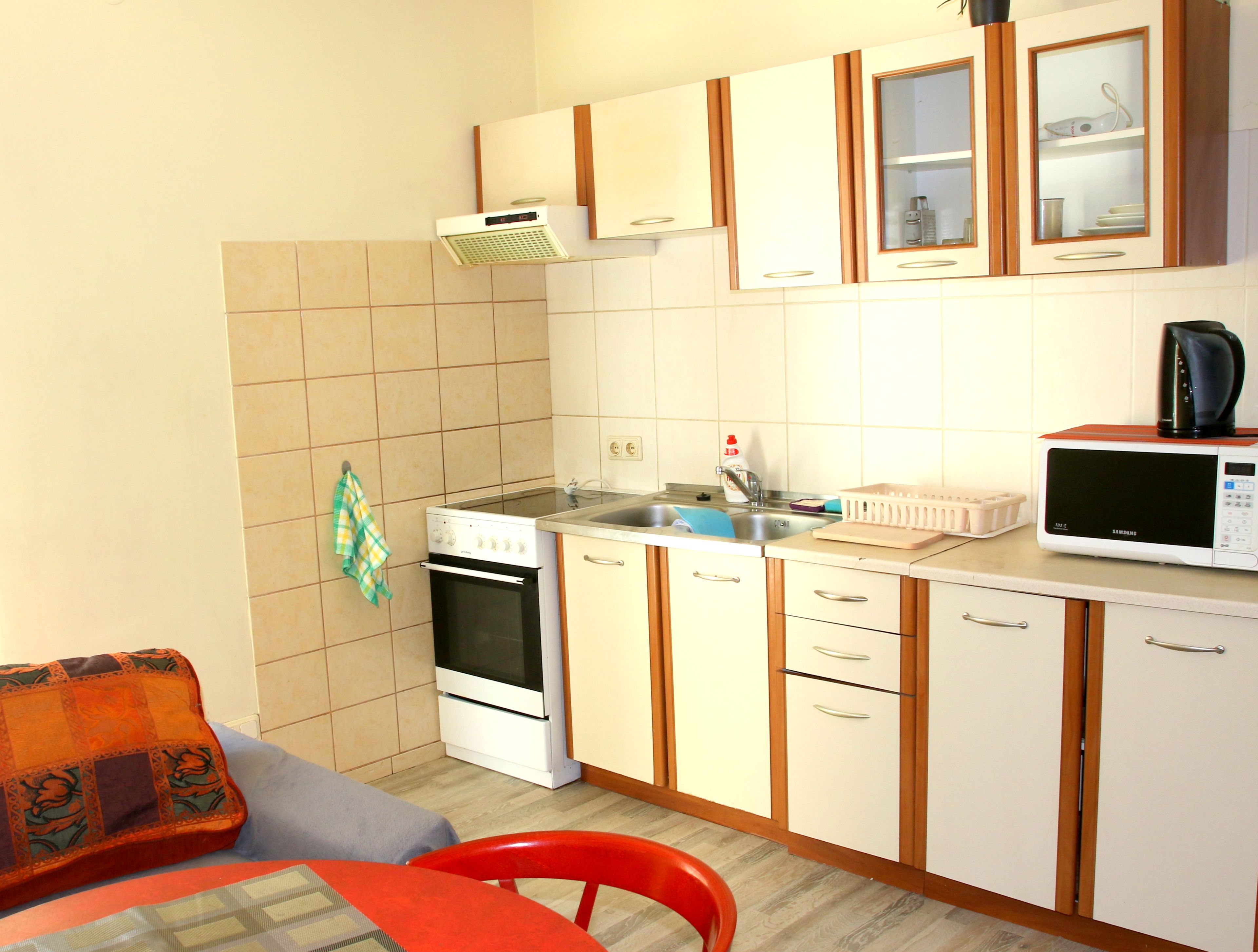 Una cocina compacta con armarios blancos, estufa, microondas y pileta.