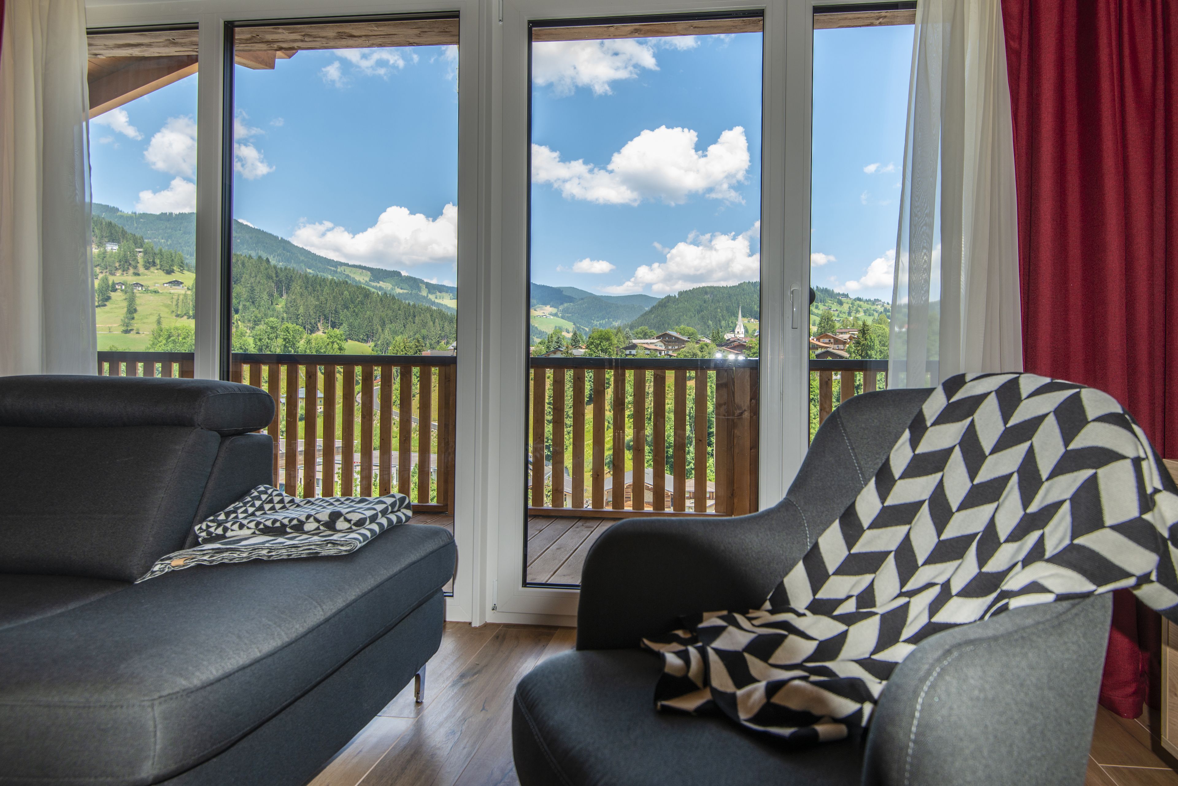 Quarto com sofá e poltrona voltados para janelas amplas com vista para colinas verdes e céu limpo.