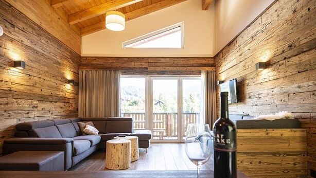 A cozy room with a wooden interior, a sofa, a small wooden table, and a wine bottle on a table. - Appartement Dorf Wagrain Alpenleben (Wagrain)