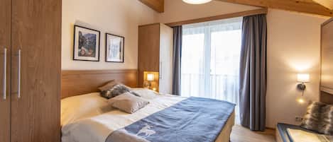 A bedroom with a large bed, wooden ceiling beams, and a window with curtains.