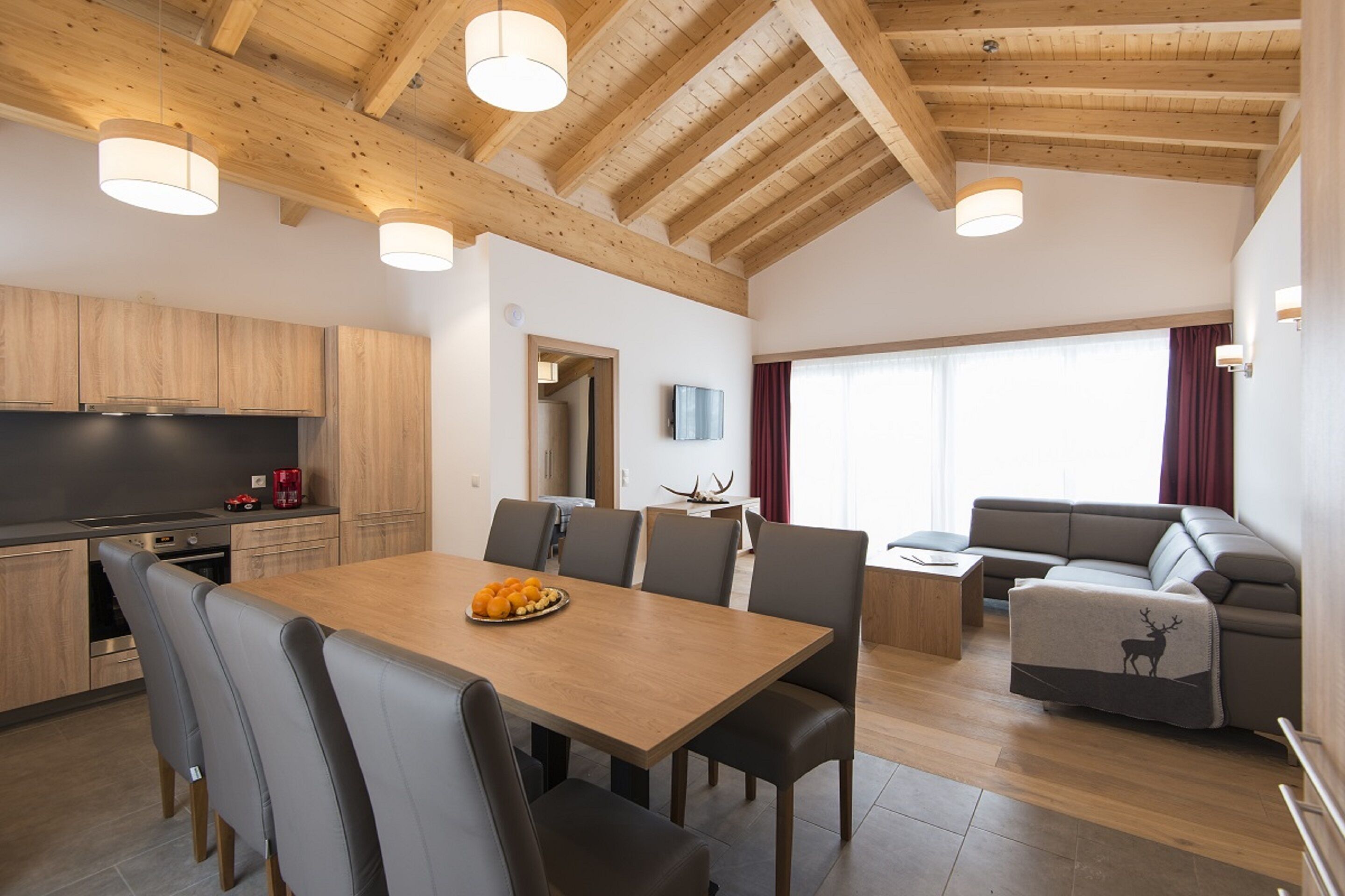 Una cocina moderna con armarios de madera, una mesa de comedor con sillas y una sala de estar con un sofá y un televisor.