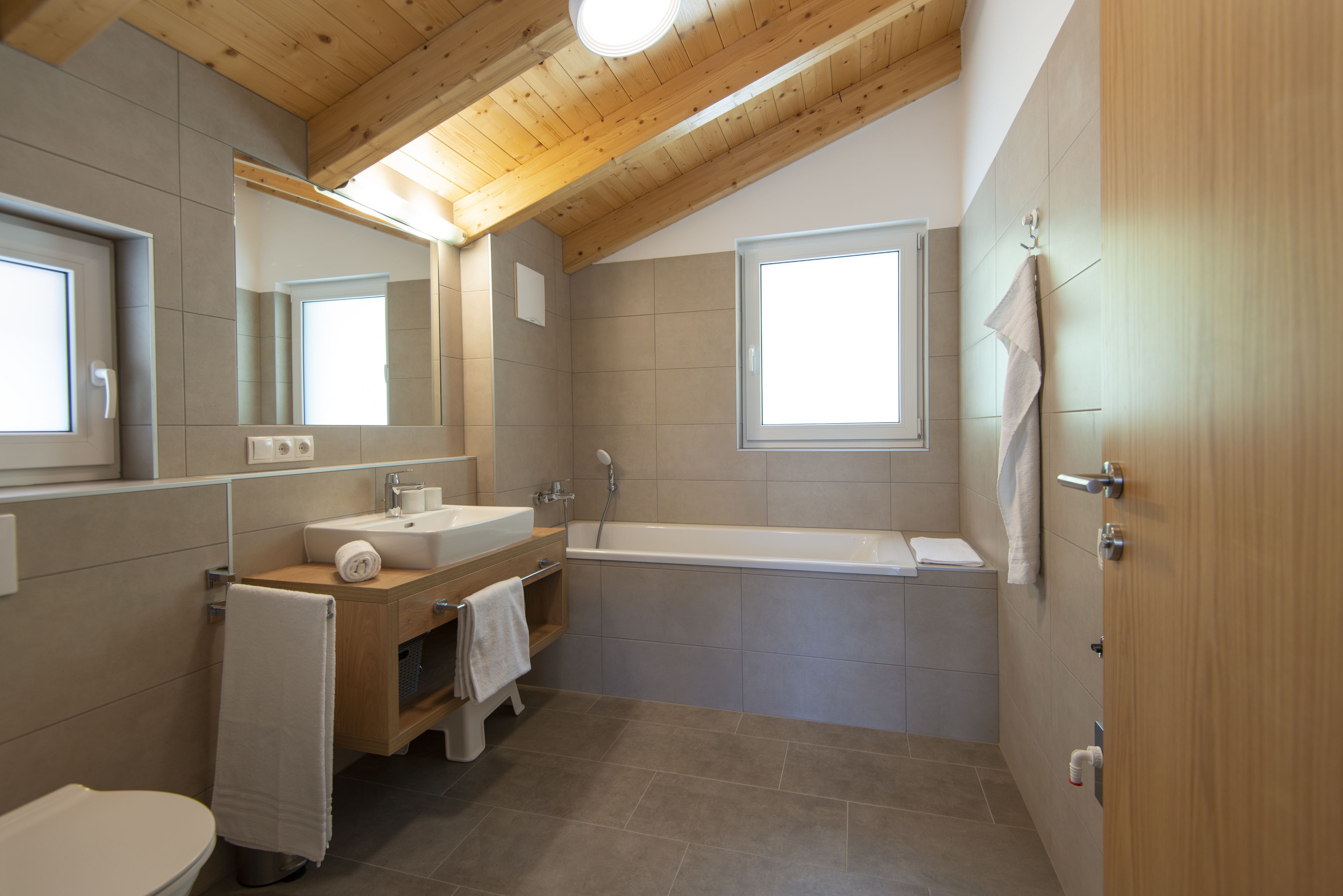 Een moderne badkamer met een houten plafond, een bad, een wastafel en een toilet.