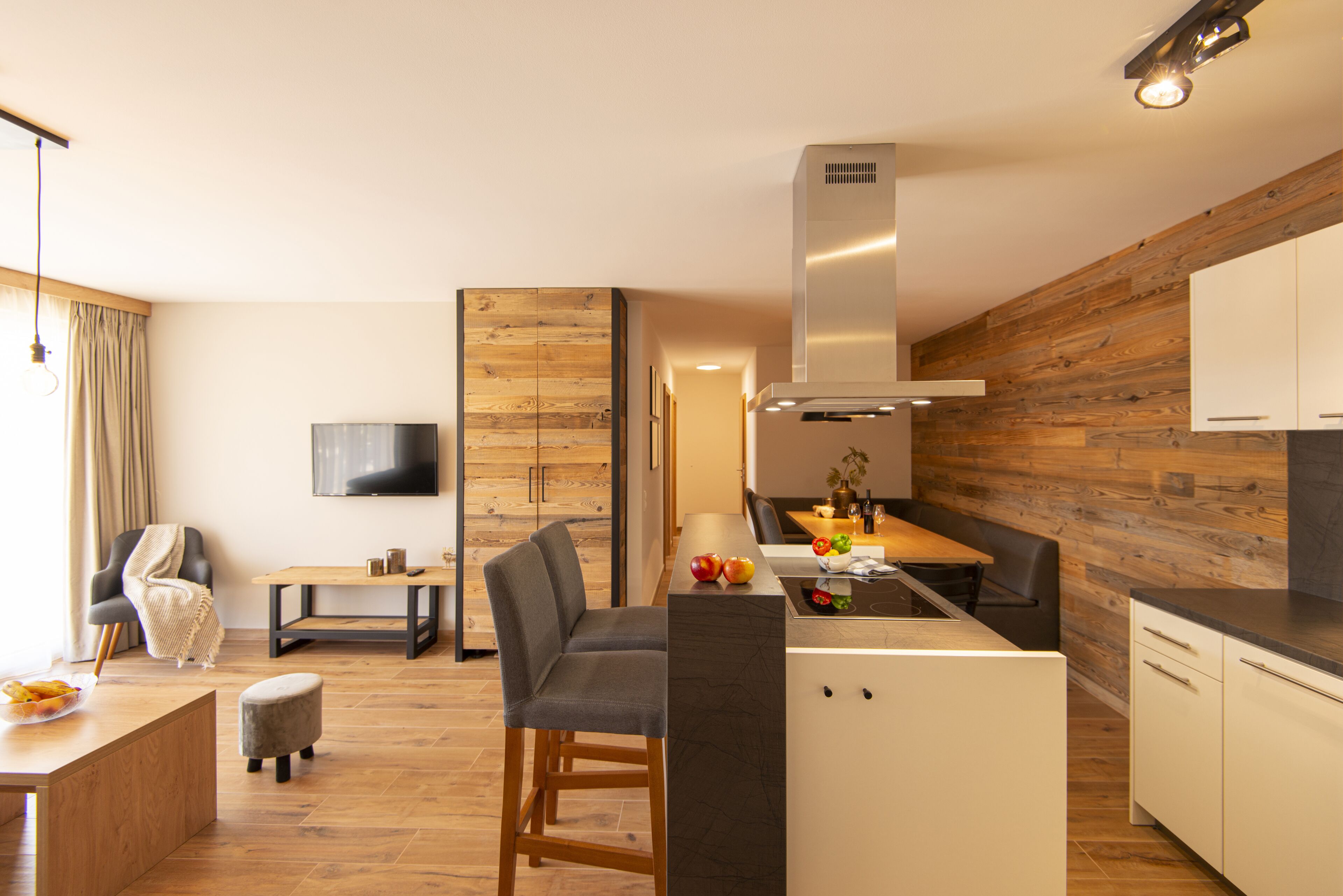 Eine moderne Küche mit Holzelementen, ein Essbereich mit Tisch und Stühlen sowie ein an der Wand befestigter Fernseher.
