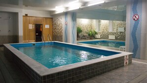 An indoor swimming pool with a tiled border, a wooden sauna door, and a no swimming sign.