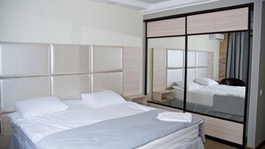 A hotel room with a large bed, a wardrobe with a mirror, and a bedside table.