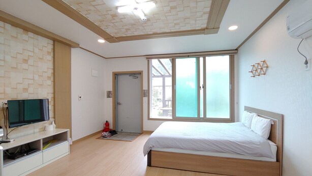 Un dormitorio moderno con una cama de madera, un televisor sobre un mueble blanco y un ventanal con vistas.
