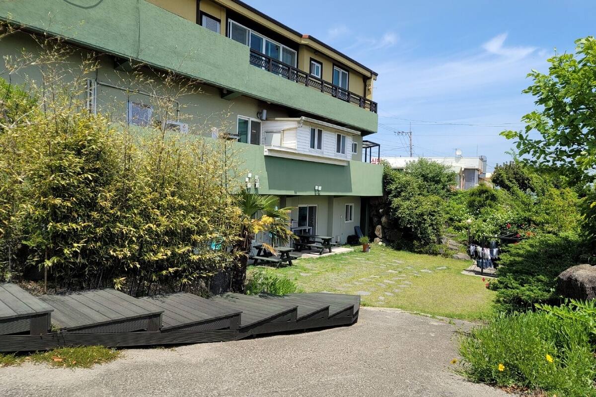 Ein mehrstöckiges Gebäude mit grüner Fassade, Außenbereich mit Sitzgelegenheiten und einem Kiesweg.