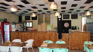 Interior de restaurante con paneles de madera, techo a cuadros y una barra con varios objetos. Mesas y sillas dispuestas para comer.