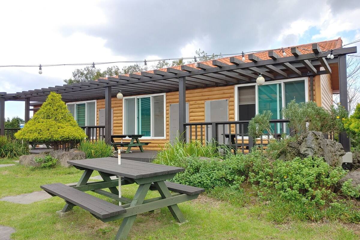 Eine Holzhütte mit überdachter Veranda, Picknicktisch und einem ordentlich beschnittenen Baum.