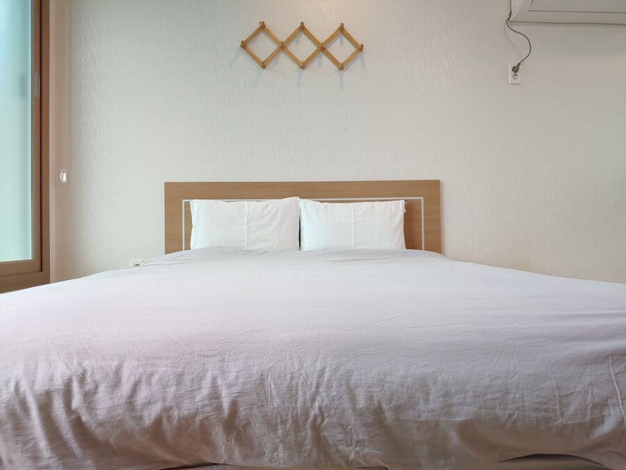 A neatly made bed with a wooden headboard, white bedding, and a simple wall decoration above it.