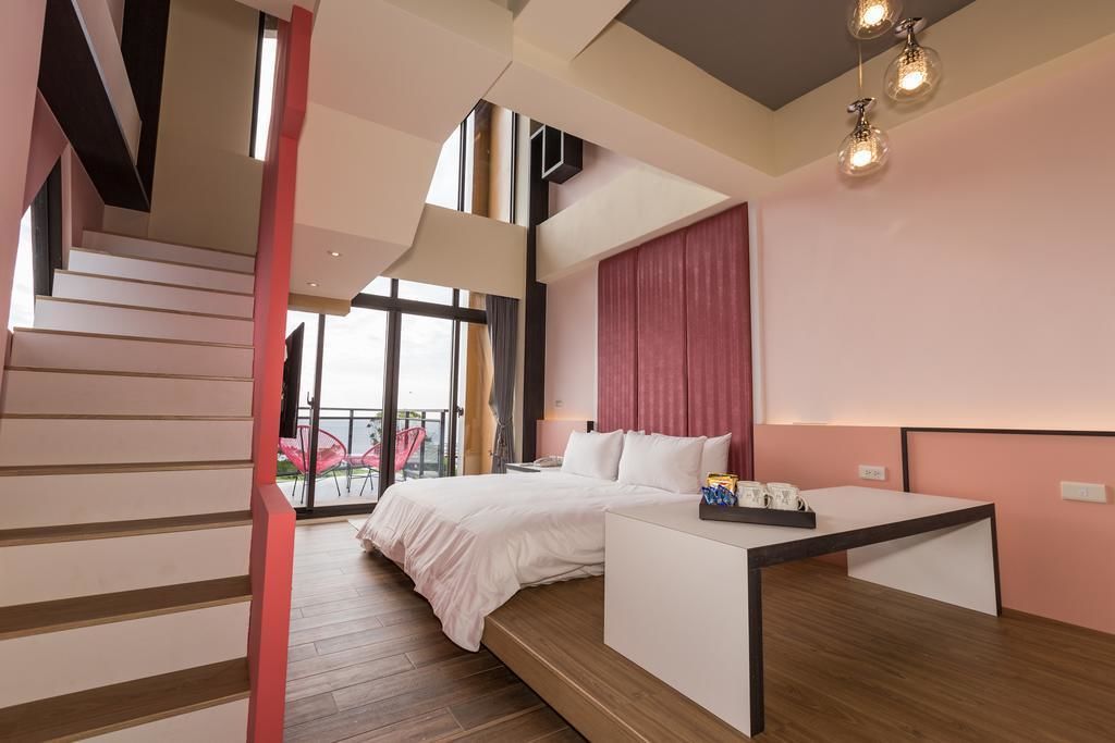 A modern hotel room with a large bed, a desk, and a staircase leading to an outdoor area.