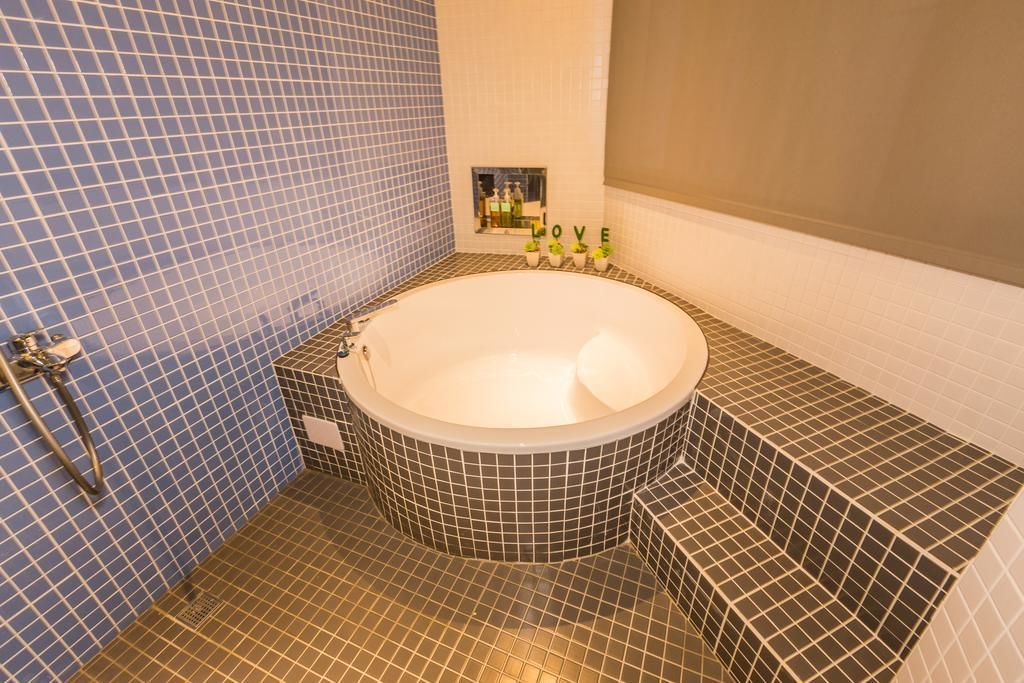 A bathroom with a large bathtub, blue and black tiled walls, and a small shelf with toiletries.