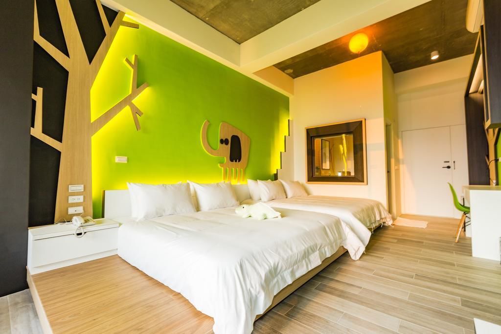 A modern bedroom with a large bed, a green accent wall, and a wooden floor.