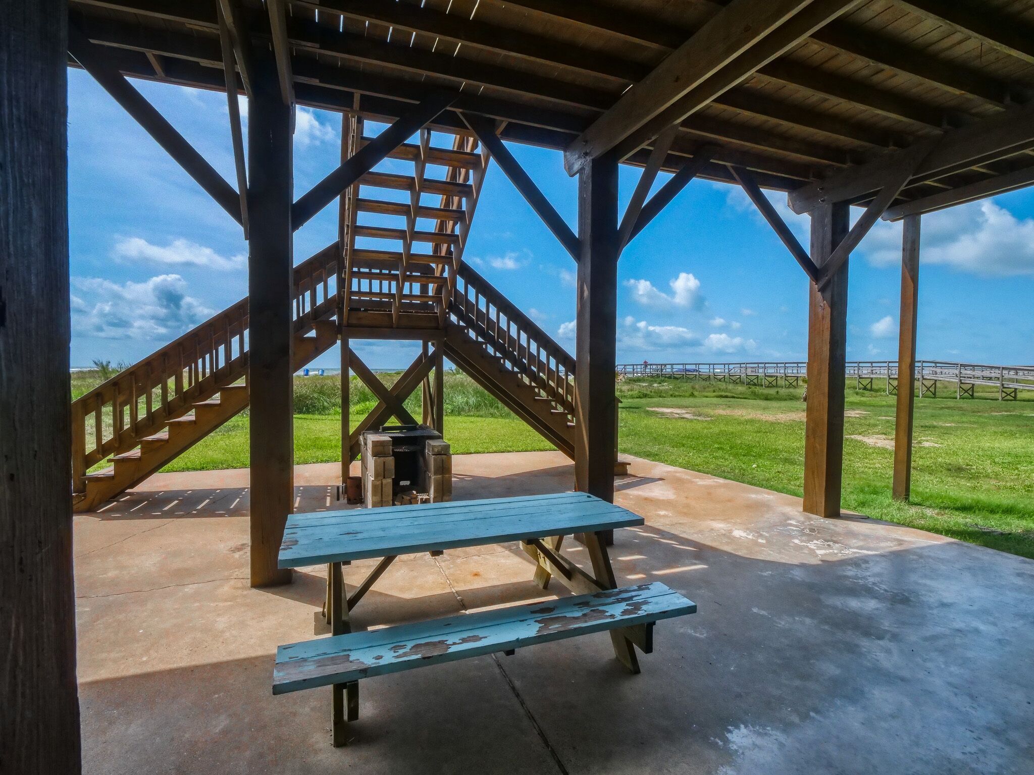 Un espace pique-nique abrité, avec un escalier en bois menant à un point de vue, des tables de pique-nique et un sol en béton.