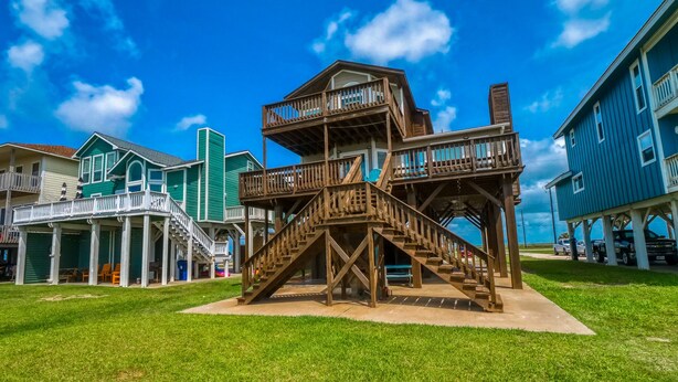 A wooden structure with multiple levels and stairs, surrounded by residential buildings. - Beach Front Home Seconds Away From The Beach (Freeport)