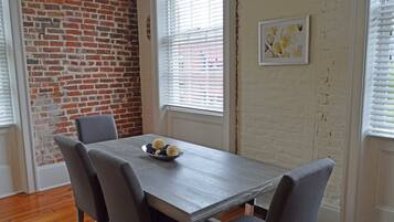 Een eetgedeelte met een bakstenen muur, een tafel met stoelen en een schaal eten.