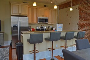 Una cocina moderna con refrigerador de acero inoxidable, microondas y estufa. Hay tres taburetes de bar y una pequeña isla con un lavamanos.