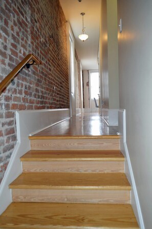 A wooden staircase with a brick wall on one side and a white railing. - "Margaux" Fully renovated 2 bed / 2 bath  Walk to WWII, Superdome, Convention Center, Cruise Port (New Orleans)