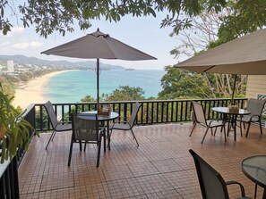 Une terrasse avec une table et des chaises, un grand parasol et une vue sur une plage et l’océan.