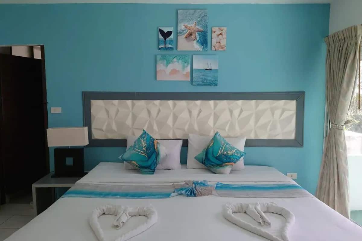 A hotel room with a bed, a headboard, artwork on the wall, and a window with curtains.