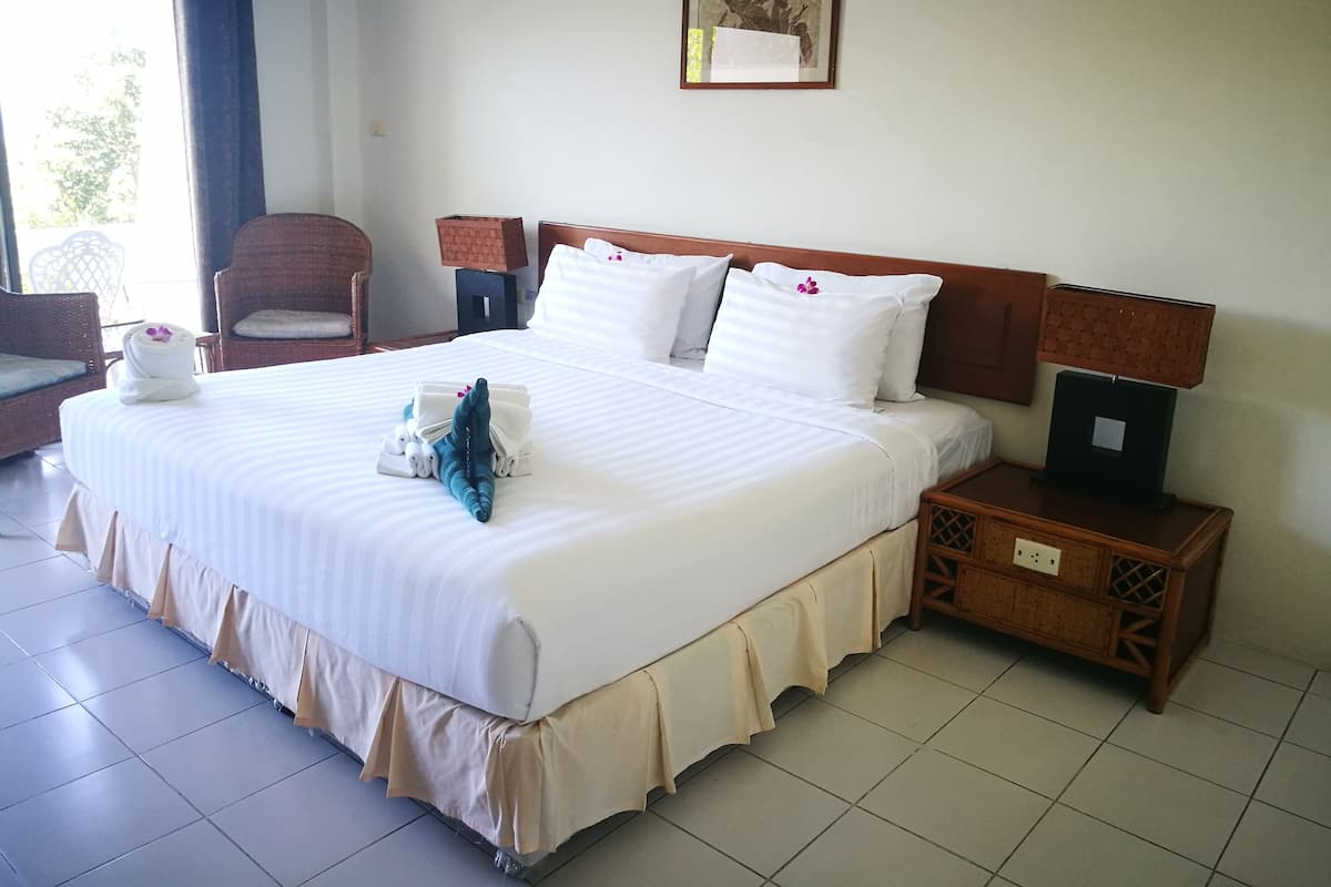 A neatly made bed with white linens and a decorative pillow, a wooden nightstand with a lamp, and a wicker chair in a hotel room.