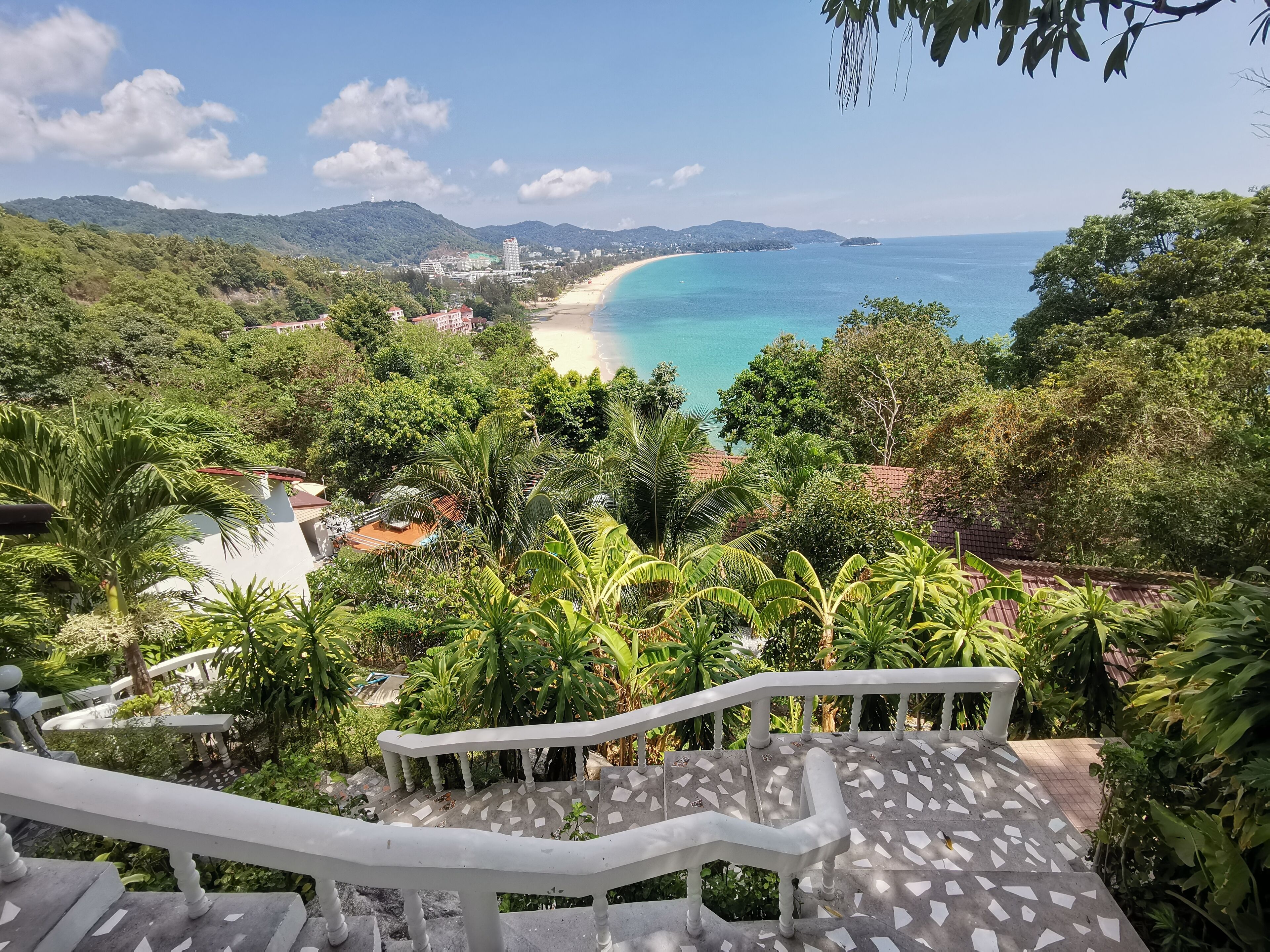Escadaria que leva a uma praia, com vista para o oceano e vegetação ao redor.