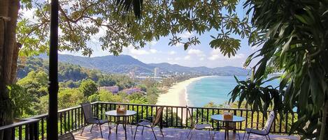 An outdoor seating area with tables and chairs, overlooking a beach and mountains.