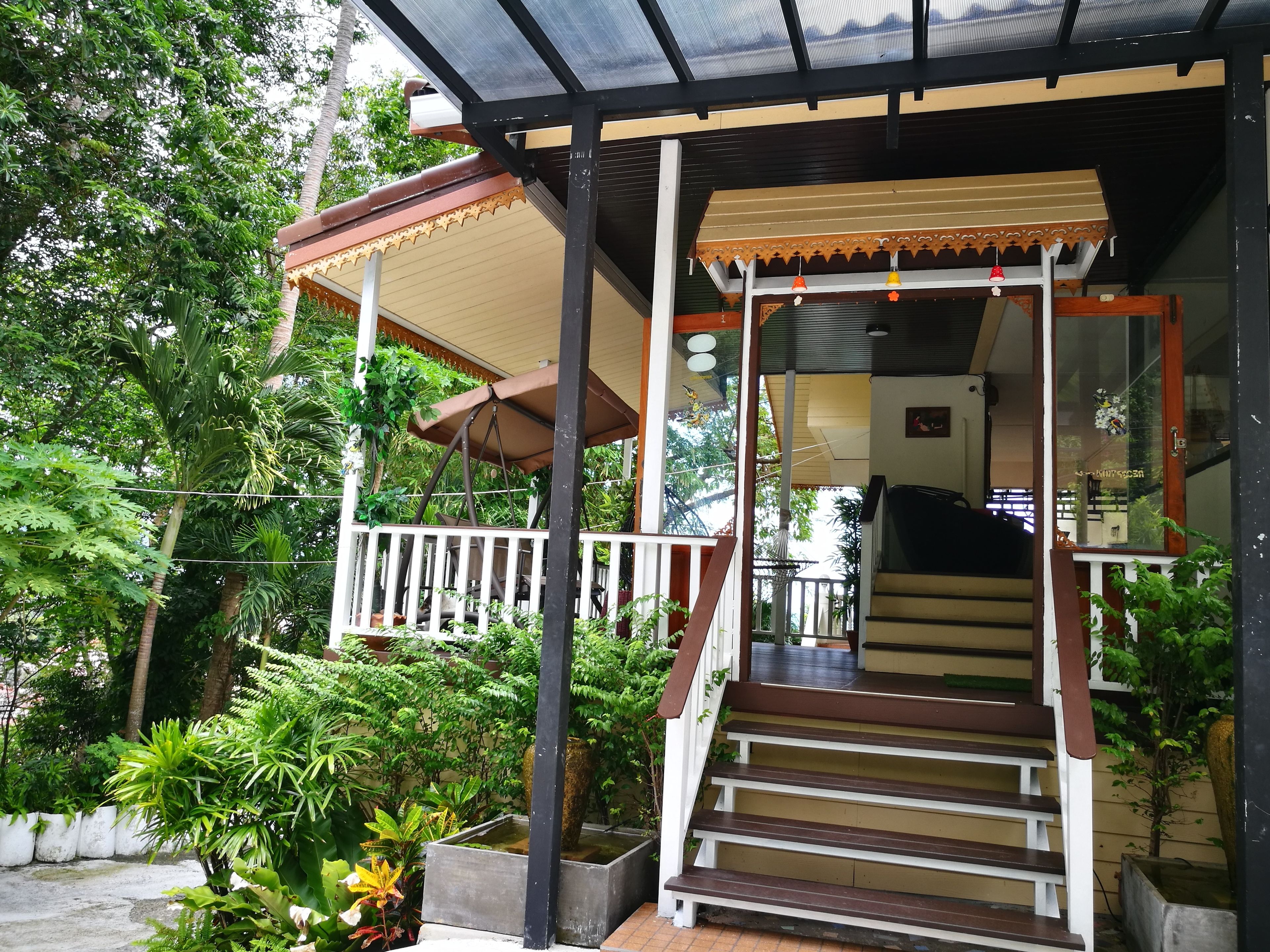 A covered outdoor staircase leading to a building with a glass door, surrounded by lush greenery.