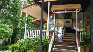 A covered outdoor staircase leading to a building with a glass door, surrounded by lush greenery.