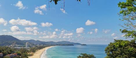 A coastal landscape with a beach, clear sky, and surrounding hills.