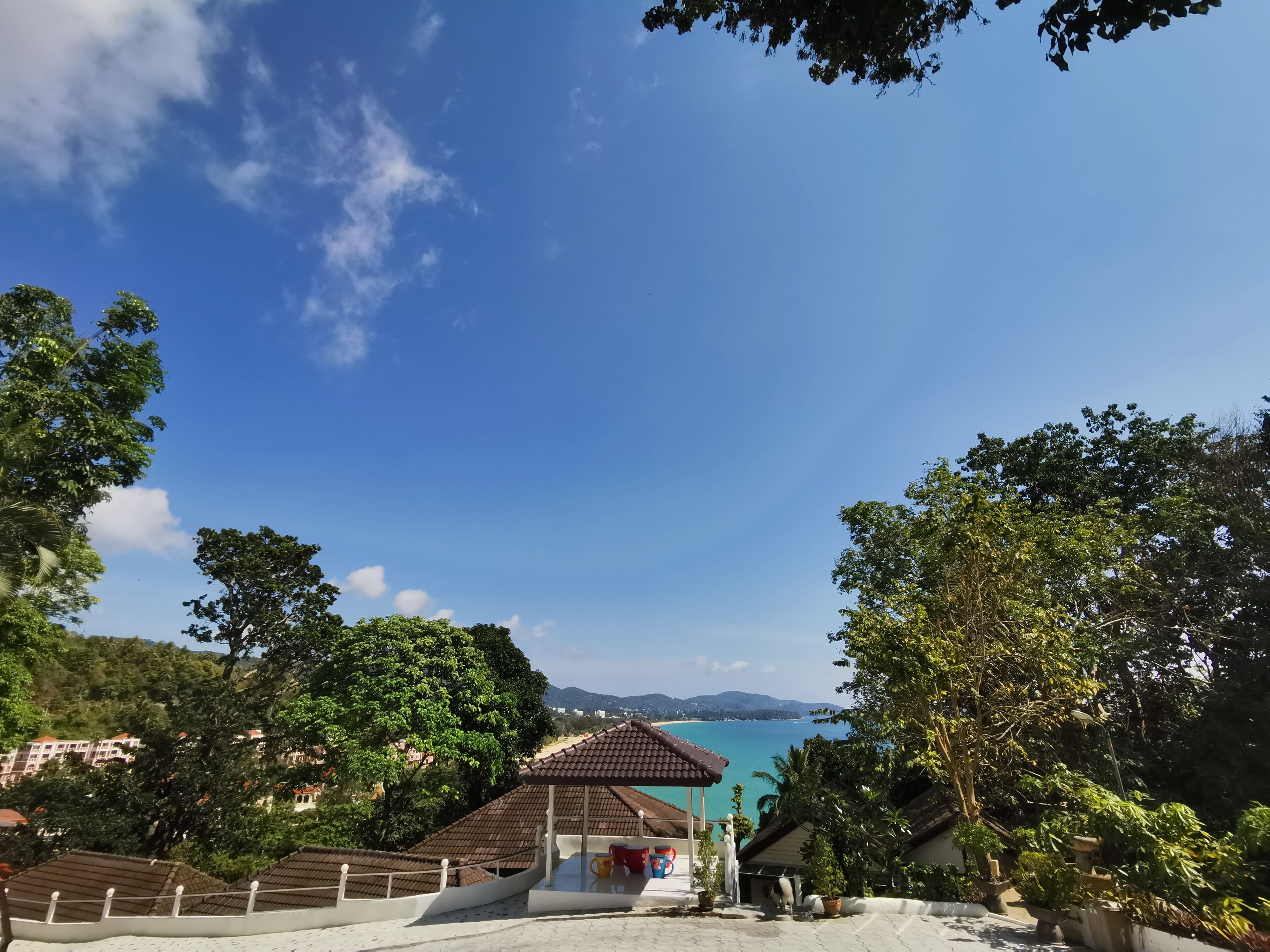 A view of a coastal area with a gazebo, lush greenery, and a clear blue sky.