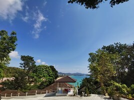 Vista de uma área costeira com um gazebo, vegetação exuberante e um céu azul límpido.