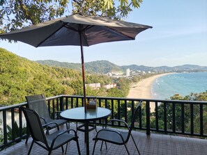 Un balcon avec une table et des chaises, donnant sur une plage et un paysage montagneux.