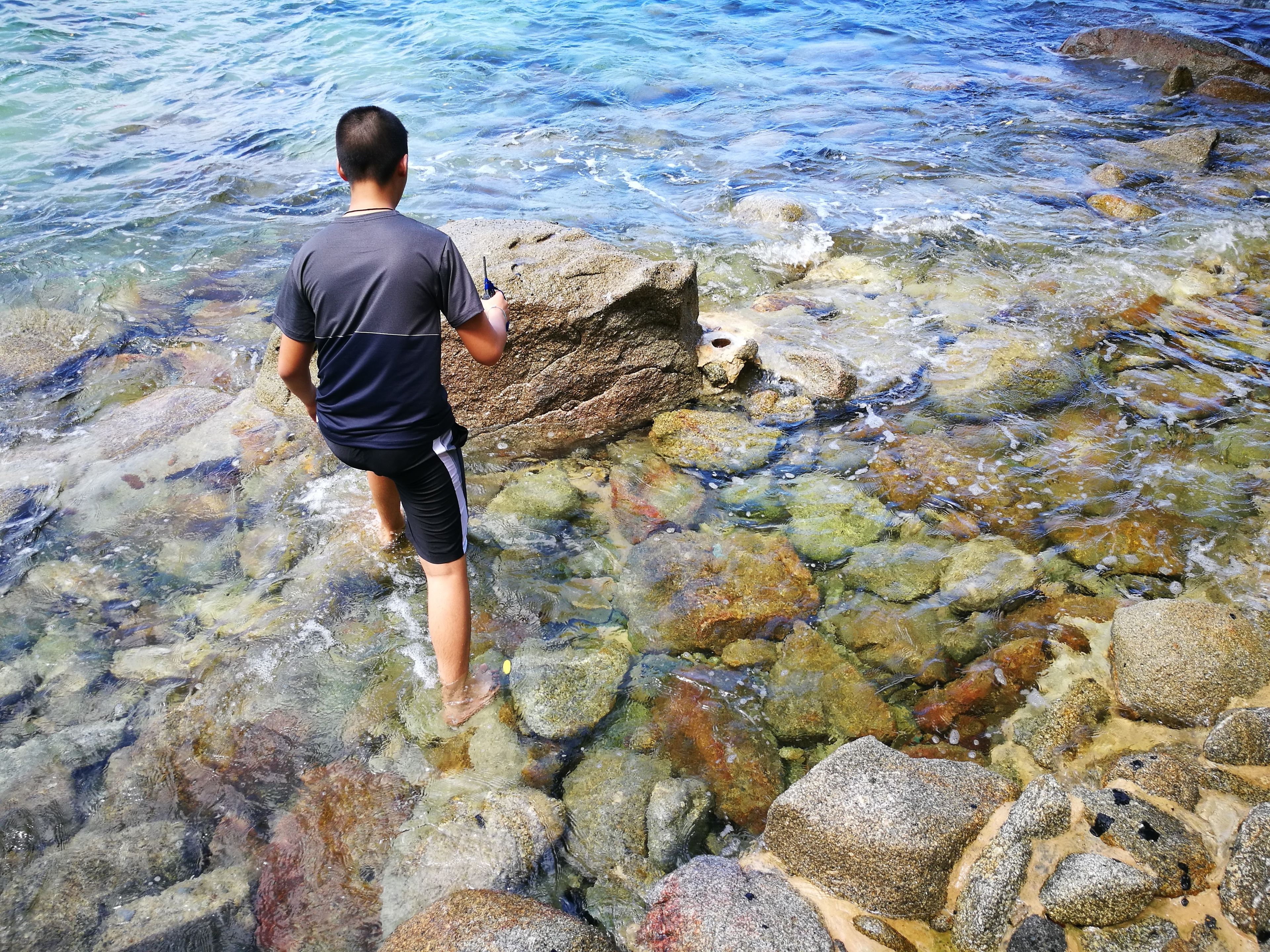 Une personne se tient au bord de l’eau, sur un terrain rocheux.