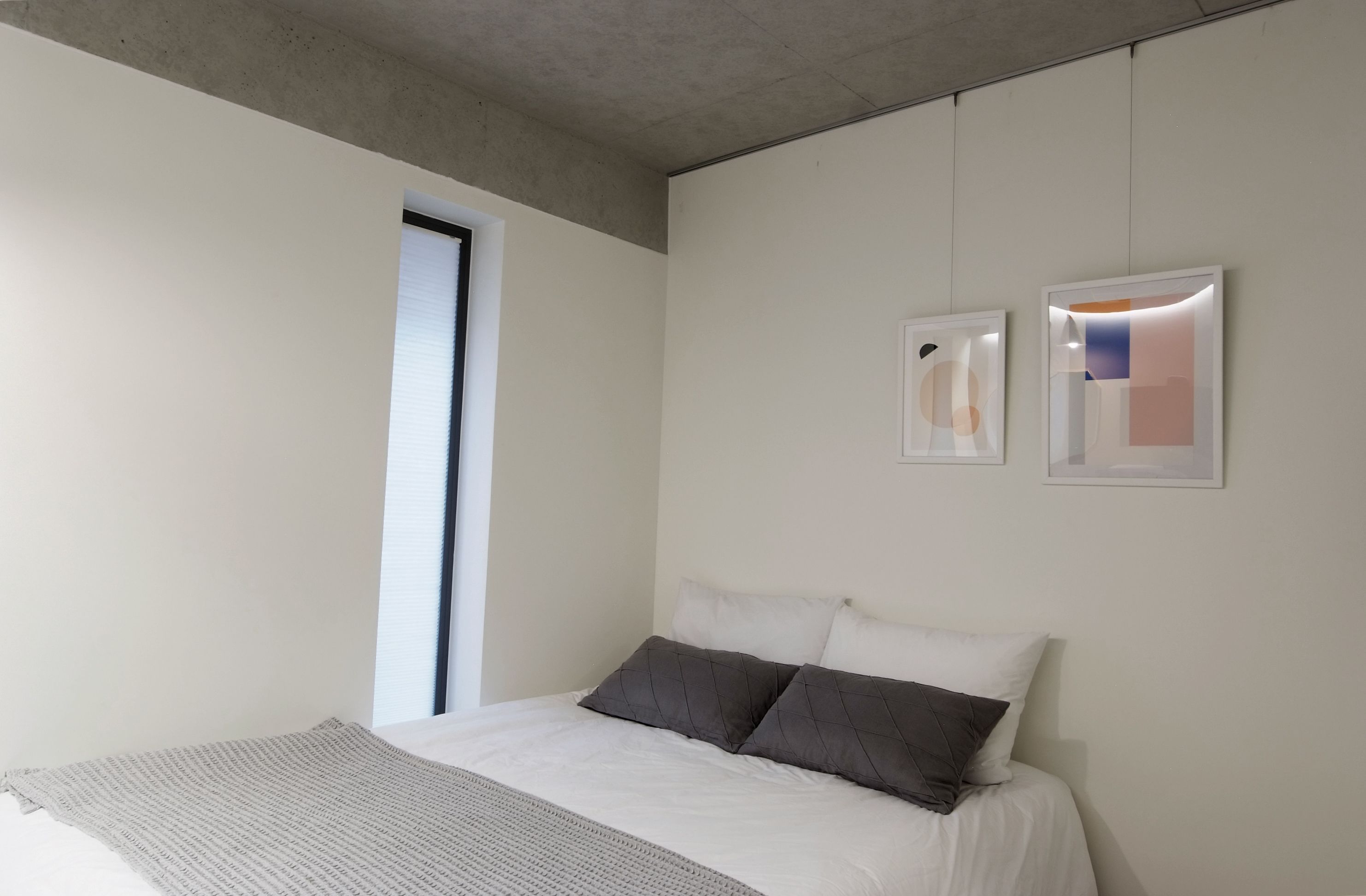 A minimalist bedroom with a bed, a window, and two framed artworks on the wall.