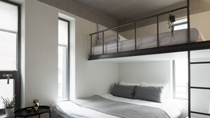 A modern bedroom with a bunk bed, a bedside table, a small stool, and a window with a view. - DW Stay Hongdae (Seoul)