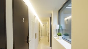 A hotel corridor with a modern design, featuring a well-lit hallway, a window with a view, and a door with a sign. - DW Stay Hongdae (Seoul)