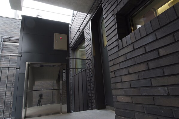 Un ascensor con puerta de vidrio, detector de incendios y barandilla metálica.