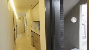 A narrow hallway with a kitchen area on the right, featuring a refrigerator, microwave, and cabinets. - DW Stay Hongdae (Seoul)