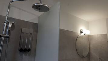 Ein modernes Badezimmer mit Dusche, einem Wandspiegel und einer Leuchte.