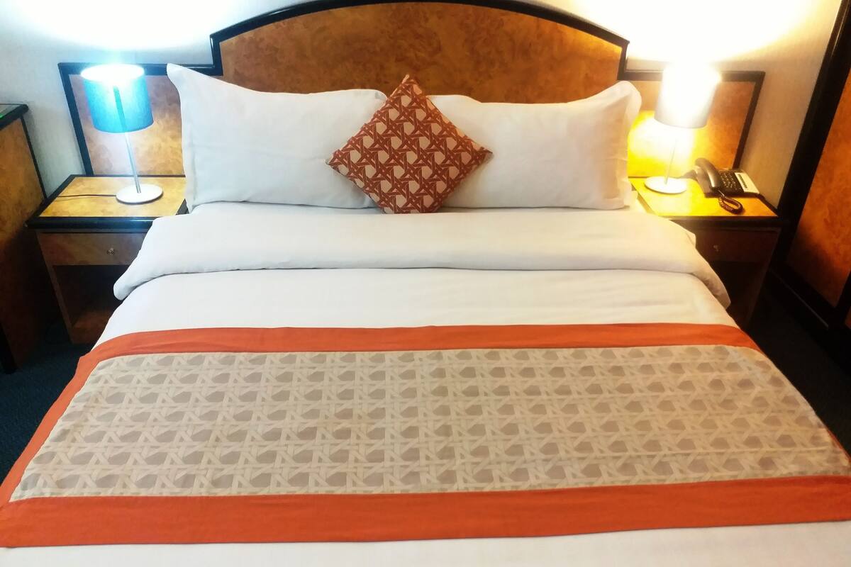 Un lit bien fait, avec une couvre-lit à motifs, deux oreillers et une tête de lit. Il y a deux tables de chevet avec des lampes et un téléphone.